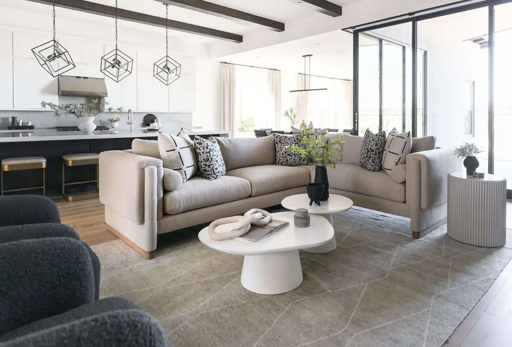 Taupe living room with round stone tables and open plan kitchen in background